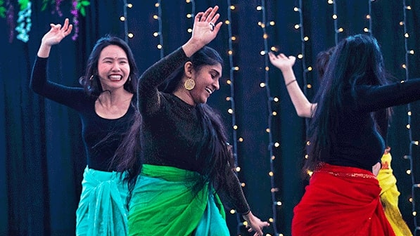 International-student-expo Three students seen dancing on stage at the International Student Expo while wearing black long-sleeved tops, and bright skirts that are blue and green. red and yellow.