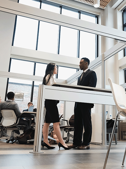 Two students dressed in business professional attire standing talking to one another.