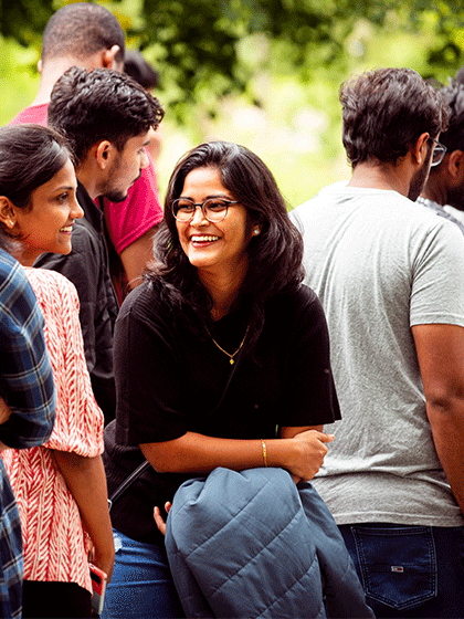 A student smiling while talking to friends, sitting outside while attending an event on campus.