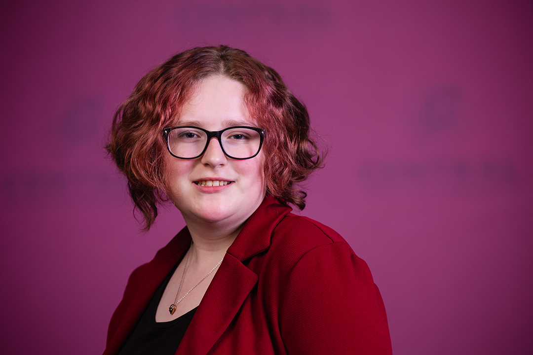 Professional headshot of Emily Guiles wearing a red blazer with black shirt while looking at the camera.