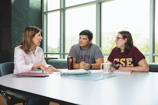 two students and professional staff member having a discussion around a table