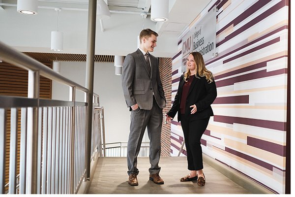 Two students in business attire talking at the top of a staircase.