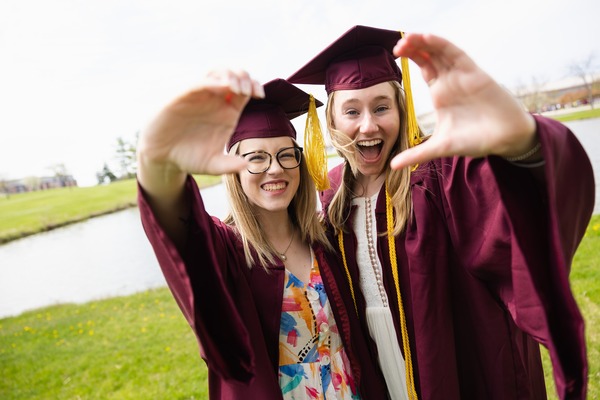 Two CMU graduates in cap and gown, posing in front of the campus pond.