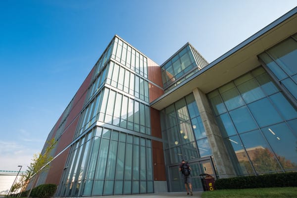 Biosciences building with glass exterior and a student walking inside.