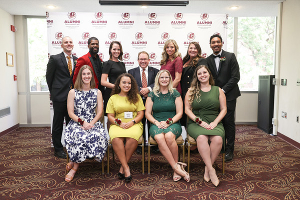 Formally dressed alumni award recipients pose with former Central Michigan University President Bob Davies in front of a CMU alumni backdrop.