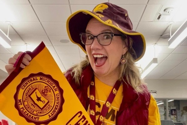 An enthusiastic person in CMU maroon and gold gear holding a pennant with the university seal on it.