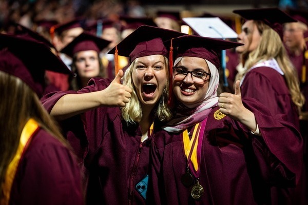 Two cheerful CMU graduates in maroon caps and gowns both giving thumbs up during a commencement ceremony.