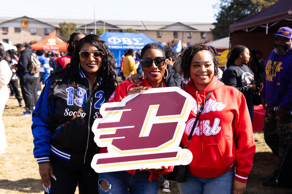 Three Central Michigan University alumni holding an Action C sign at an outdoor event.