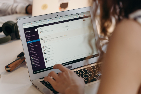 A person typing on a laptop at a desk, with a communications application displayed on the screen.