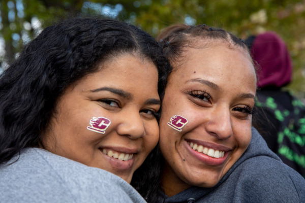 Close-up of two individuals, with maroon and gold Action C stickers on their faces, standing closely together outdoors.