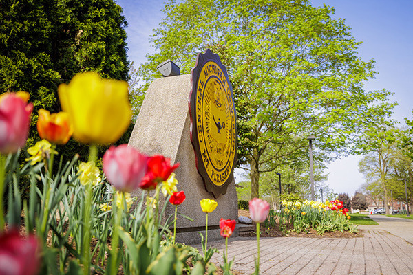 The Central Michigan University seal is surrounded by vibrant flowers on a sunny day on CMU's campus.