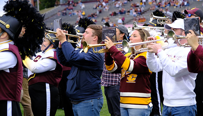 Central Michigan University marching band alumni play trumpets in unison during a football game halftime performance at Kelly/Shorts Stadium.