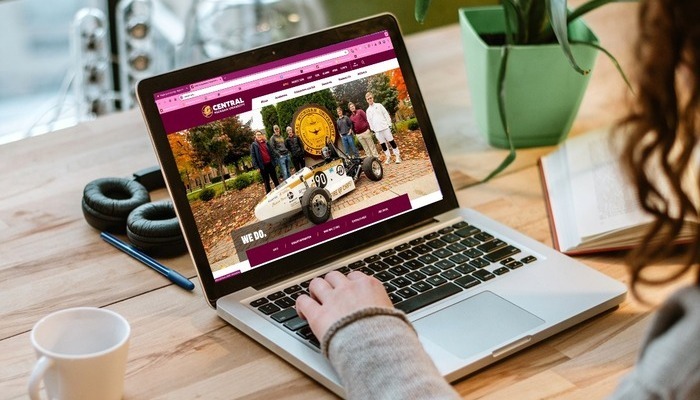 A person using a laptop displaying the Central Michigan University website.