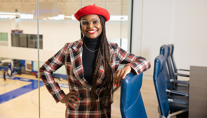 A Central Michigan University alumna posing in a plaid suit and red beret in a modern office setting.