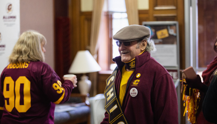 Two Central Michigan University alumni in maroon and gold apparel at an indoor CMU alumni gathering.