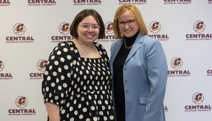 Two women pose in front of a Central Michigan University backdrop.