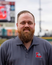 A bearded man wearing a dark gray polo shirt with a red and white 