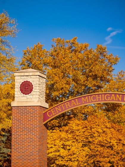 a close up of the Voisin Arch on a fall day. Orange autumn leaves are the background. The focus is on the CMU seal on a brick pillar.