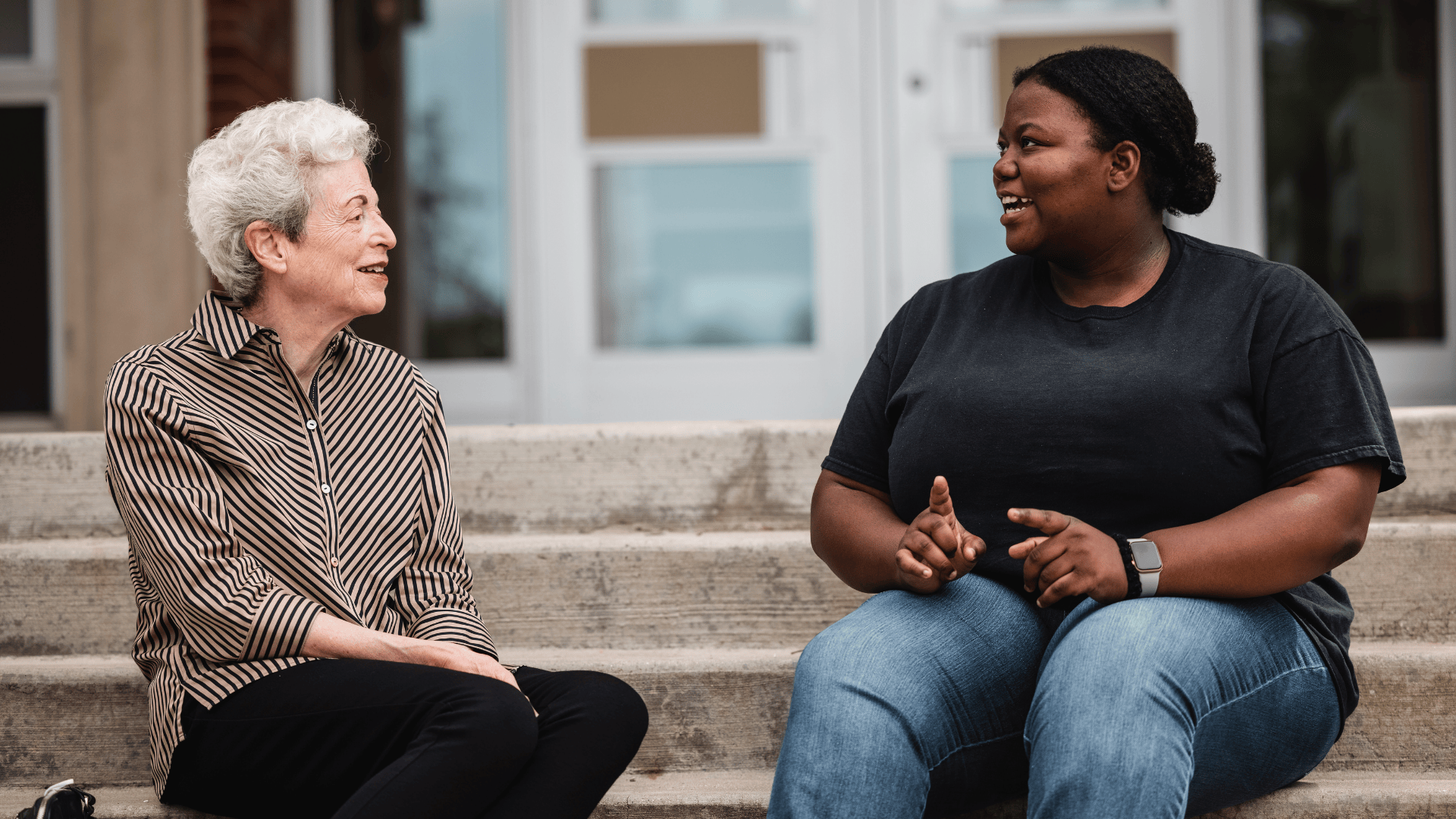 An alumnus sits with a current student on steps.