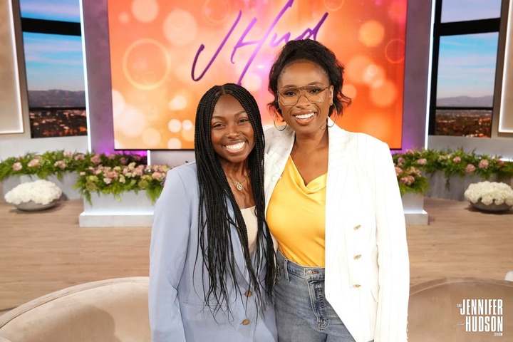 Akayla Joseph, posing with Jennifer Hudson, on the Jennifer Hudson Show set in front of a large screen.