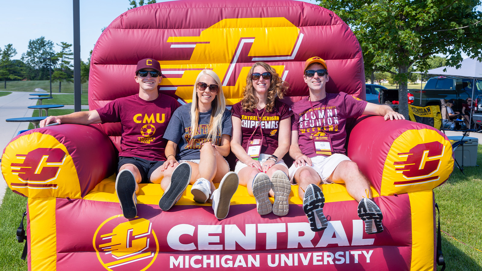 A group of four people wearing Central Michigan University shirts, sit on a large, inflatable Central Michigan University chair.