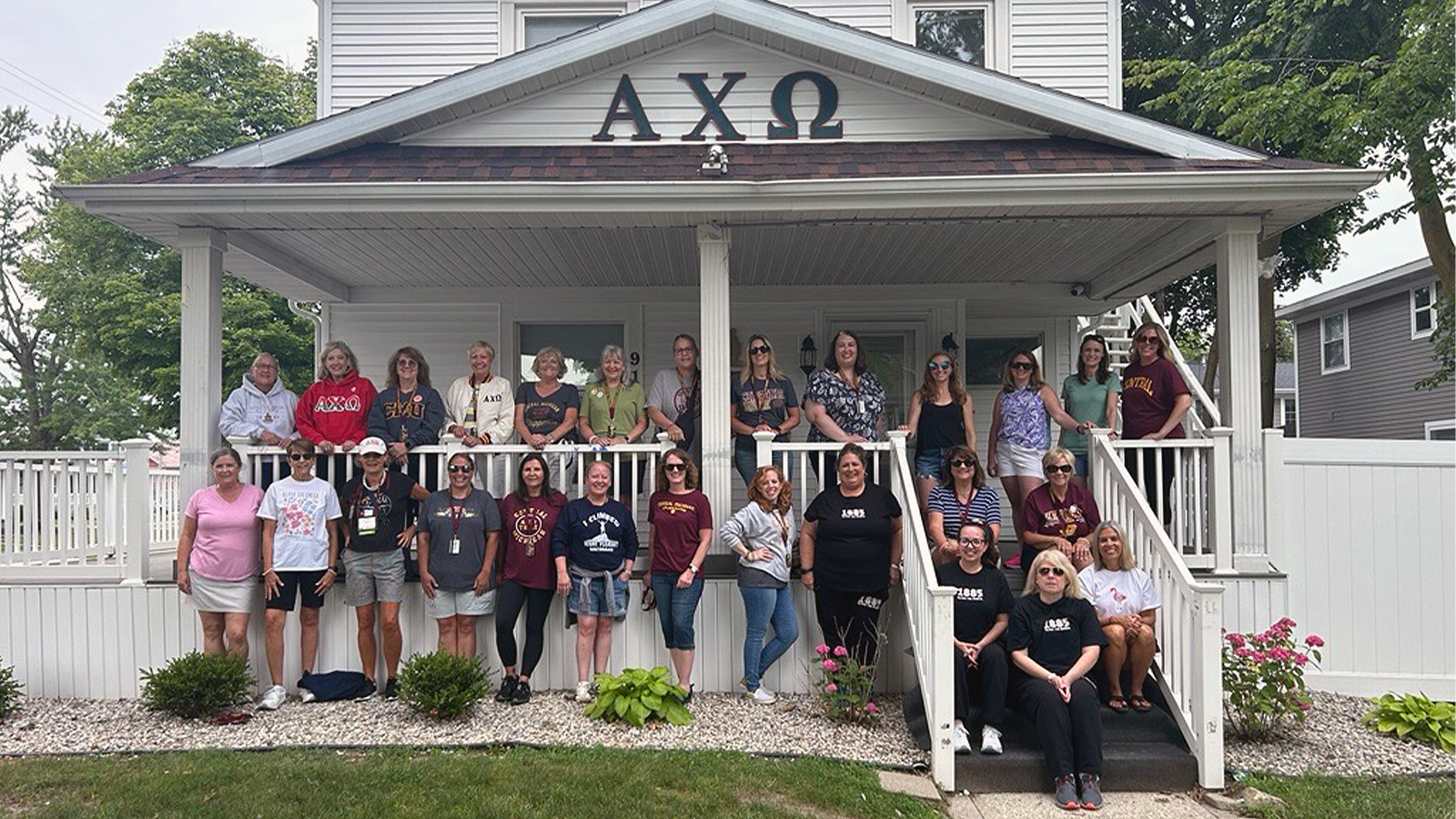 A group of women standing and sitting while posing for a picture on a porch of a sorority house.