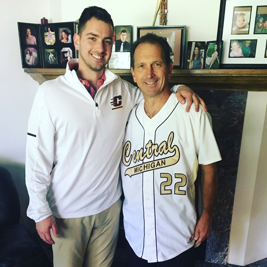 Two men wearing Central Michigan University shirts stand next to each other and smile for a picture.